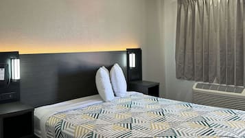 A hotel room with a bed, two bedside tables with lamps, a wall-mounted air conditioner, and a window with curtains.