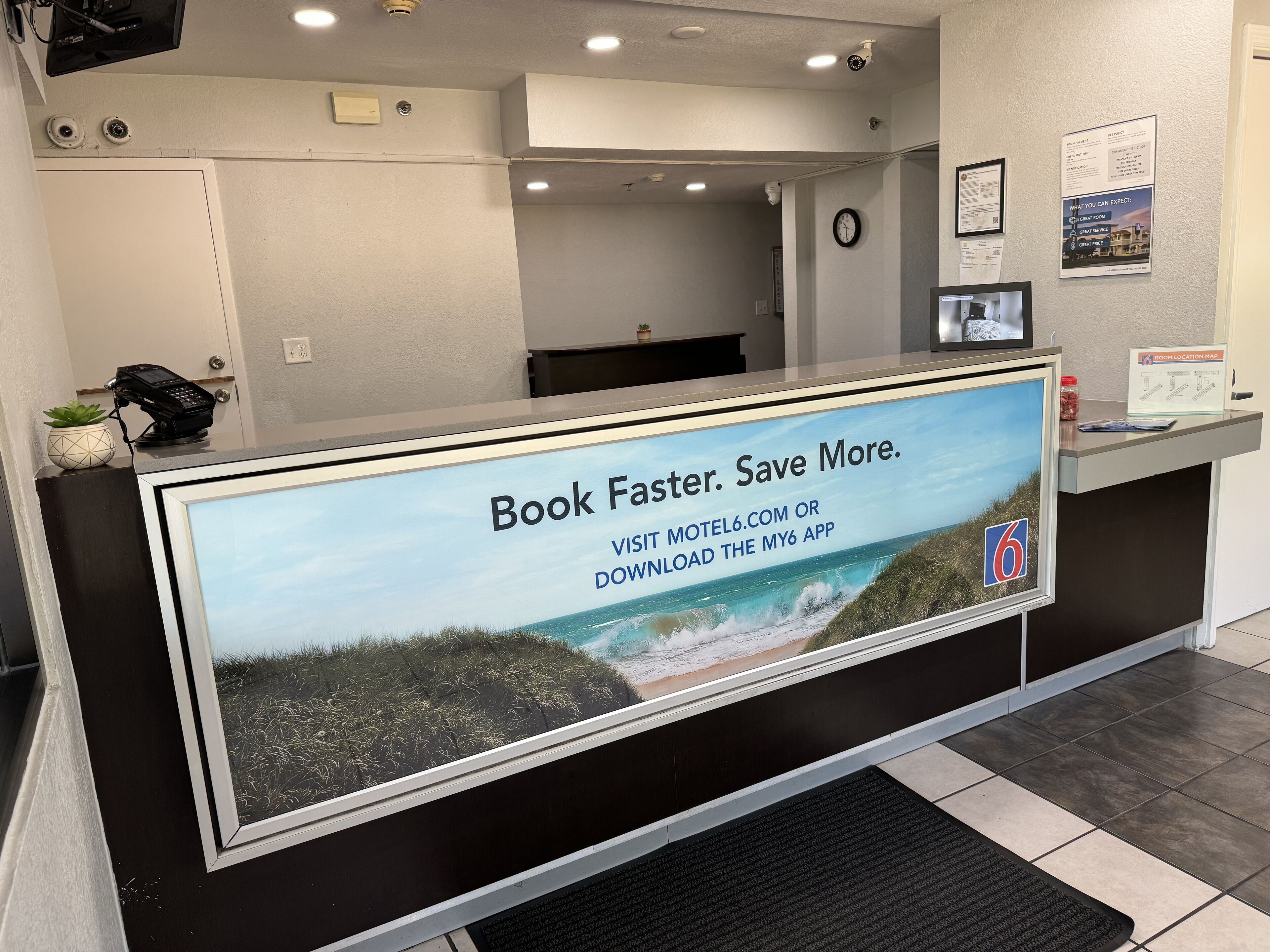 Un mostrador de recepción con una pantalla grande mostrando una escena de playa y texto que promociona una aplicación de reservas.