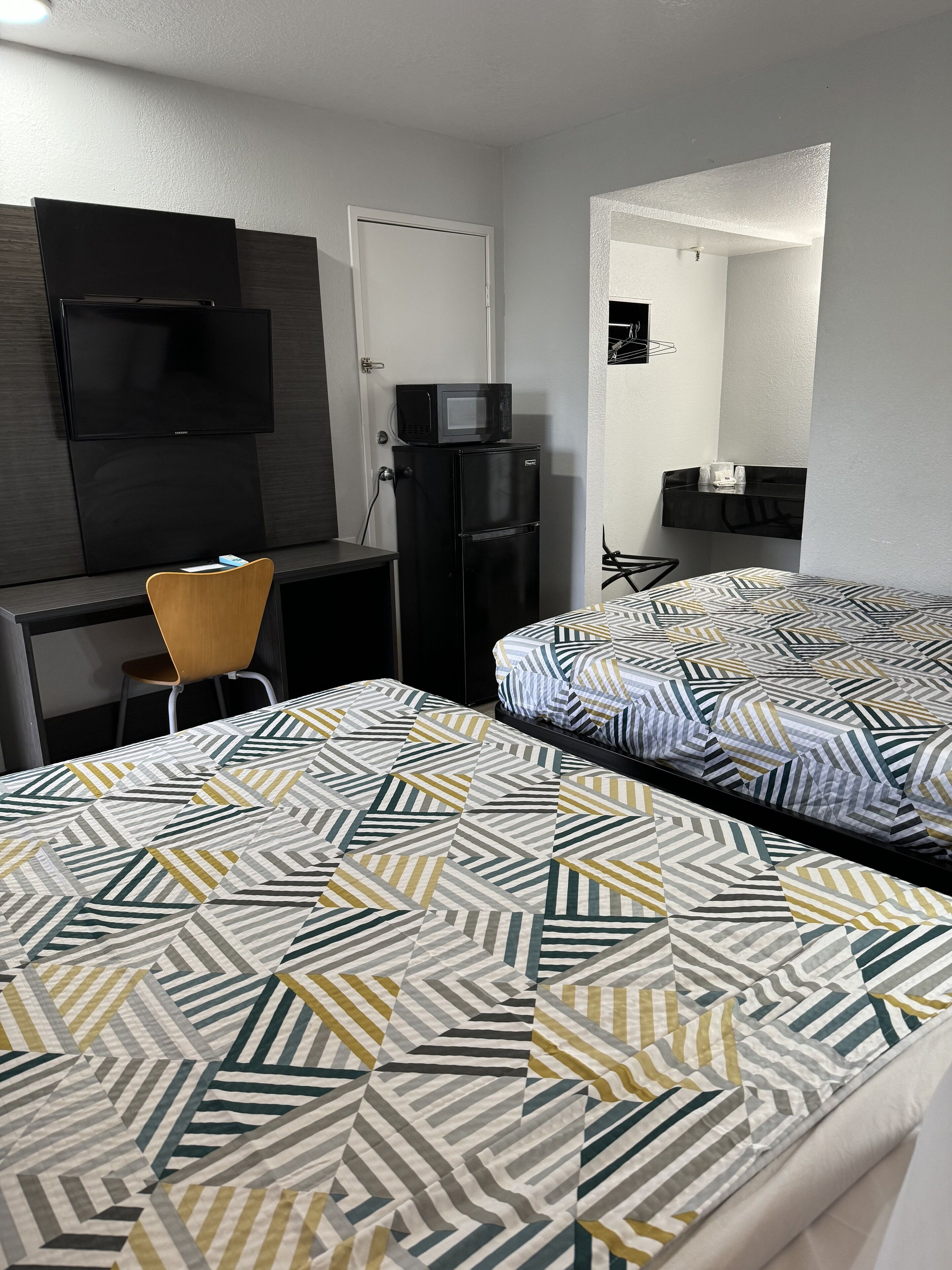 A hotel room with a bed, a desk, a chair, a TV, and a refrigerator.