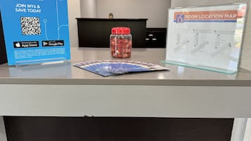 A hotel reception desk with a blue sign promoting My6 membership rates, a room location map, and a jar of snacks.