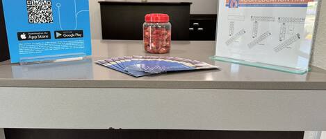 Een hotel receptiebalie met een blauw bord waarop My6 lidmaatschapstarieven staan, een plattegrond van de kamers en een pot met snacks.