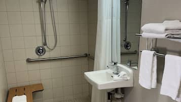 A bathroom with a shower, sink, and handrails.