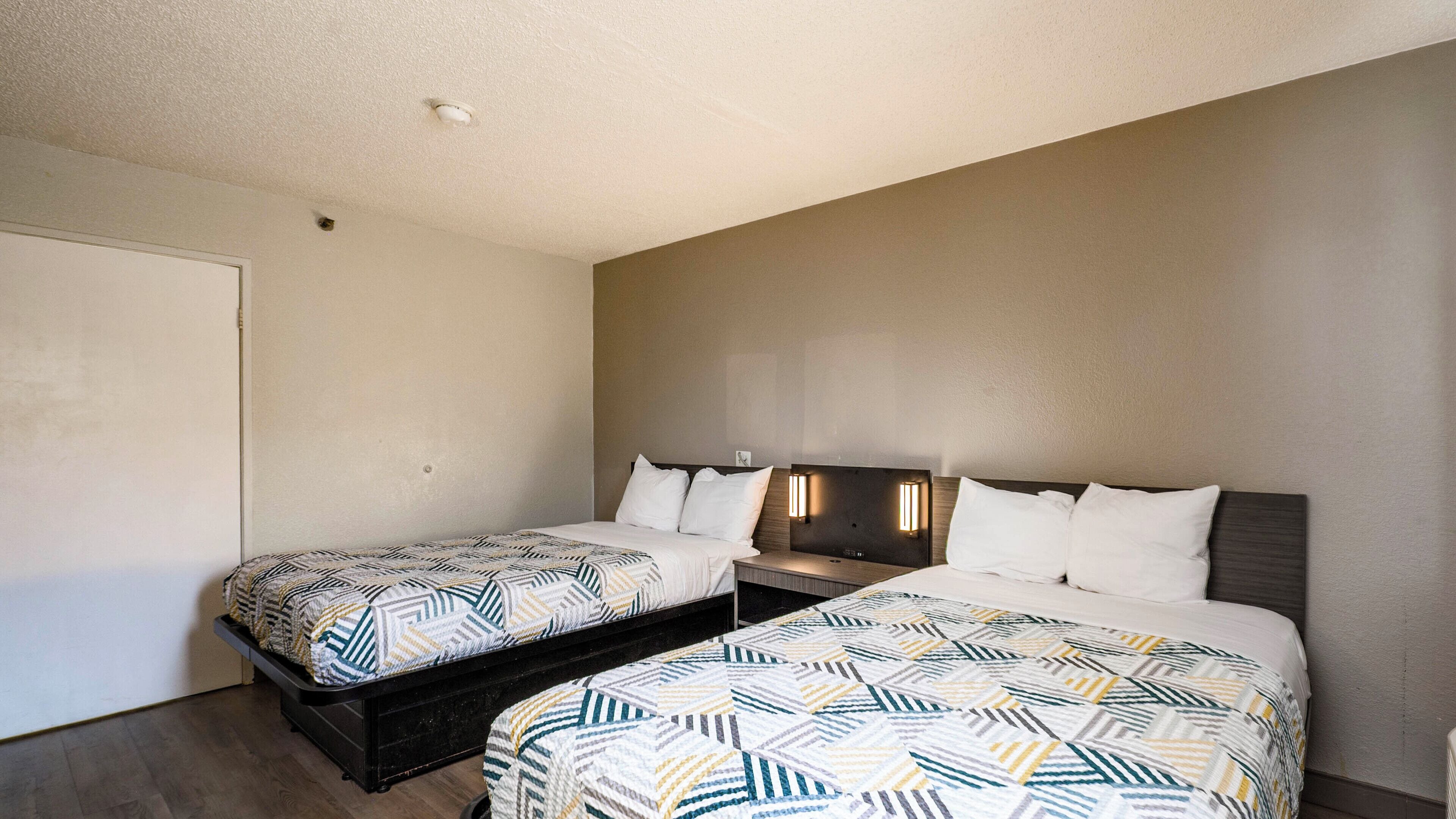 A hotel room with two beds, a wardrobe, and a nightstand with a lamp.