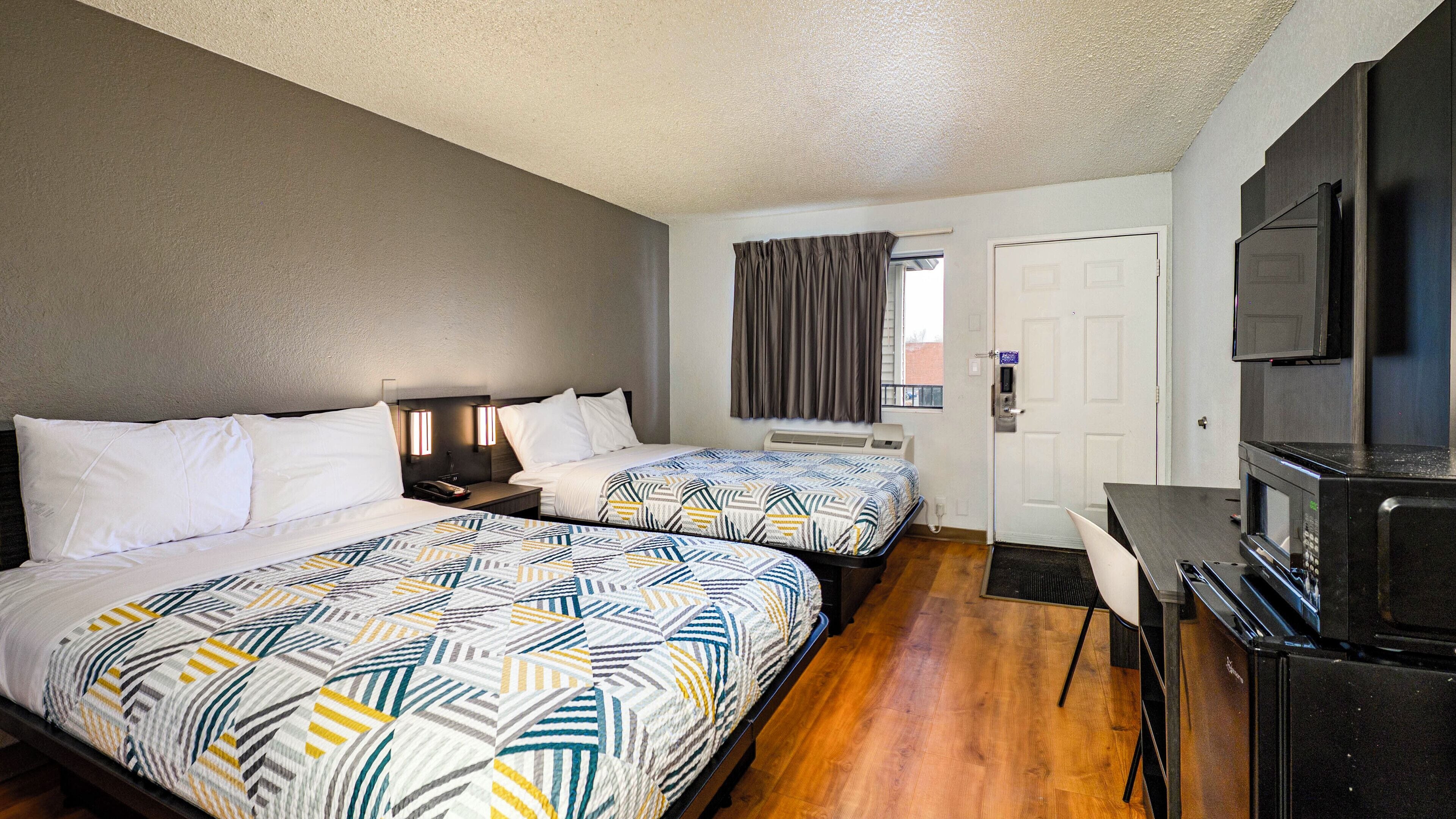 A hotel room with two beds, a desk, a TV, and a door.