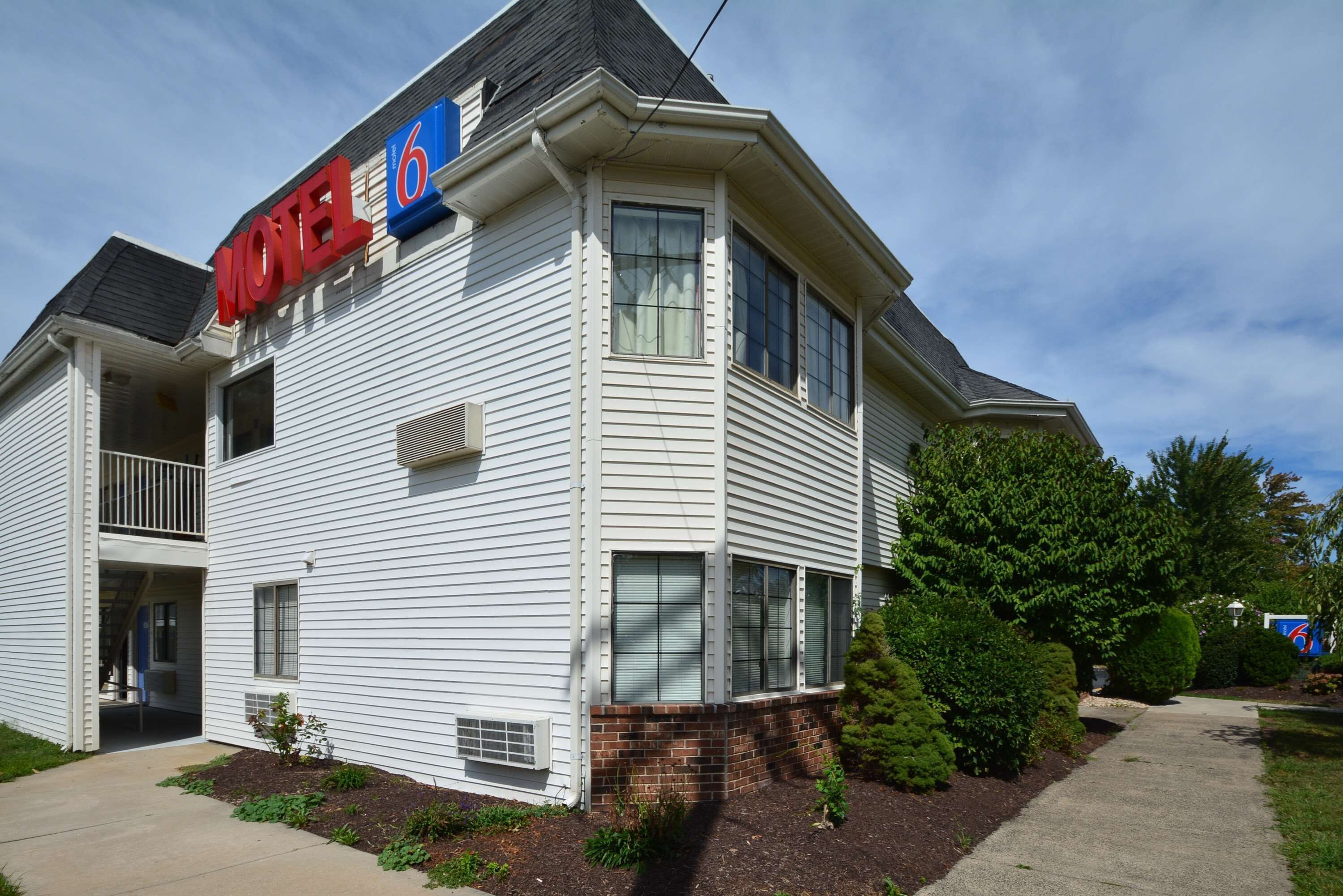 A two-story motel with a '6' sign, a balcony on the second floor, and a brick foundation.