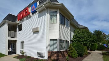 A two-story motel with a '6' sign, a balcony on the second floor, and a brick foundation.