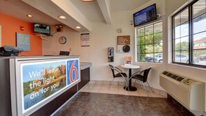 A hotel reception area with a digital screen, a clock, a sign about morning charges, and a view of parked cars outside. - Motel 6 Wethersfield, CT - Hartford (Wethersfield)