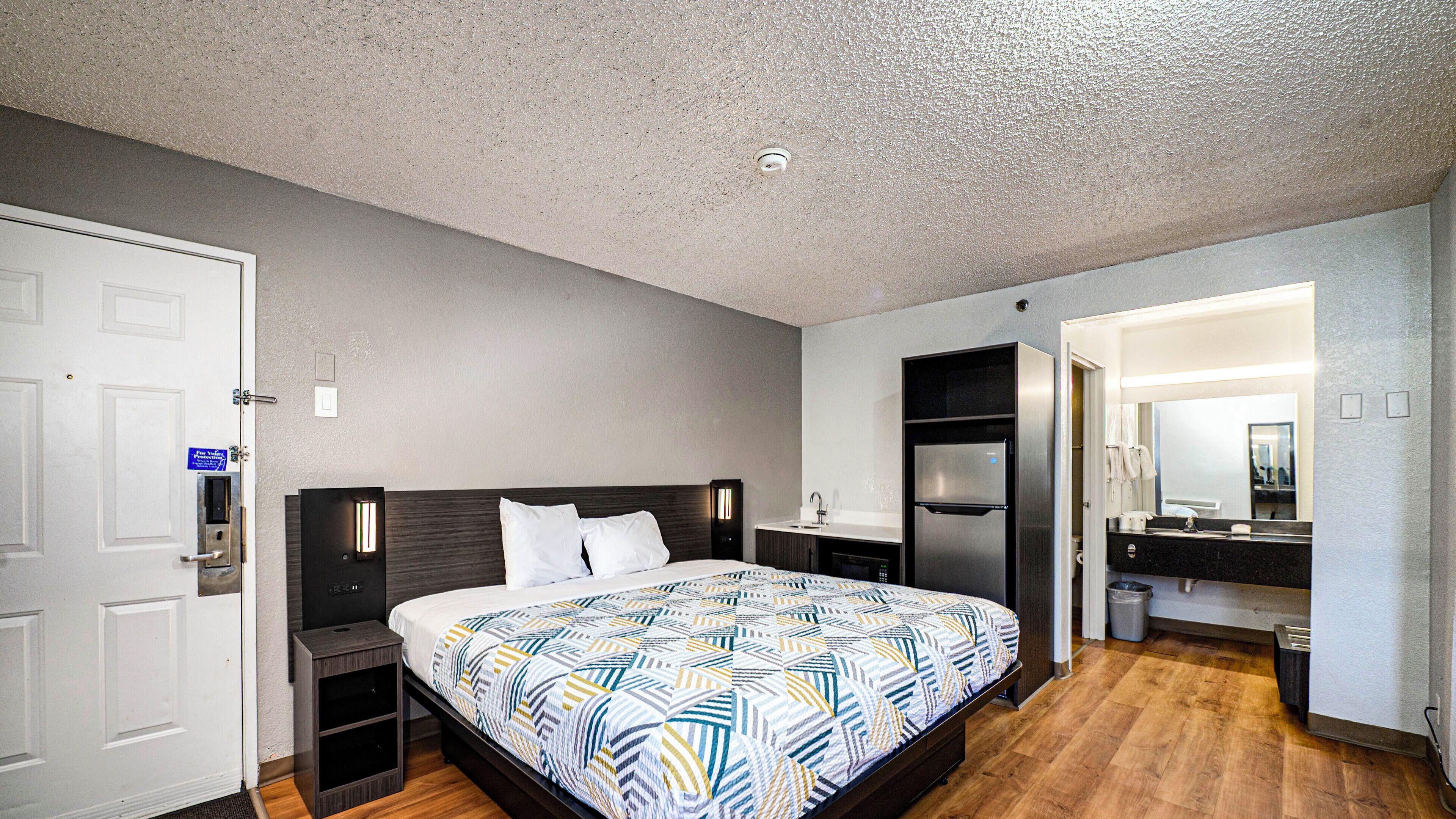 Habitación de hotel con cama, mesita de noche, armario empotrado y baño con espejo.