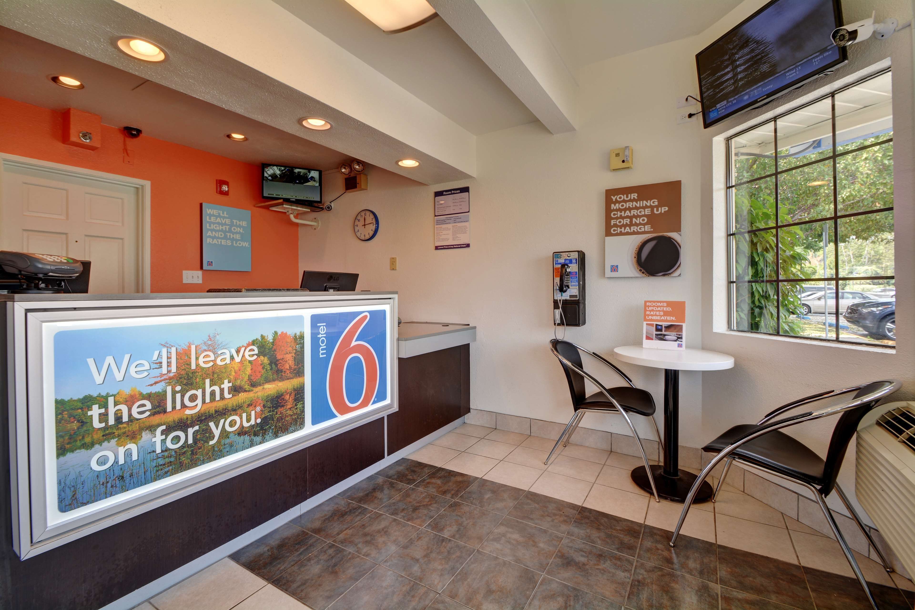 A hotel reception area with a reception desk, a clock, a television, and a window with a view of the outside.