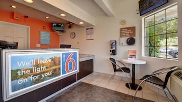 Un espace d’accueil d’hôtel comprenant un comptoir de réception, une horloge, un téléviseur et une fenêtre donnant sur l’extérieur.