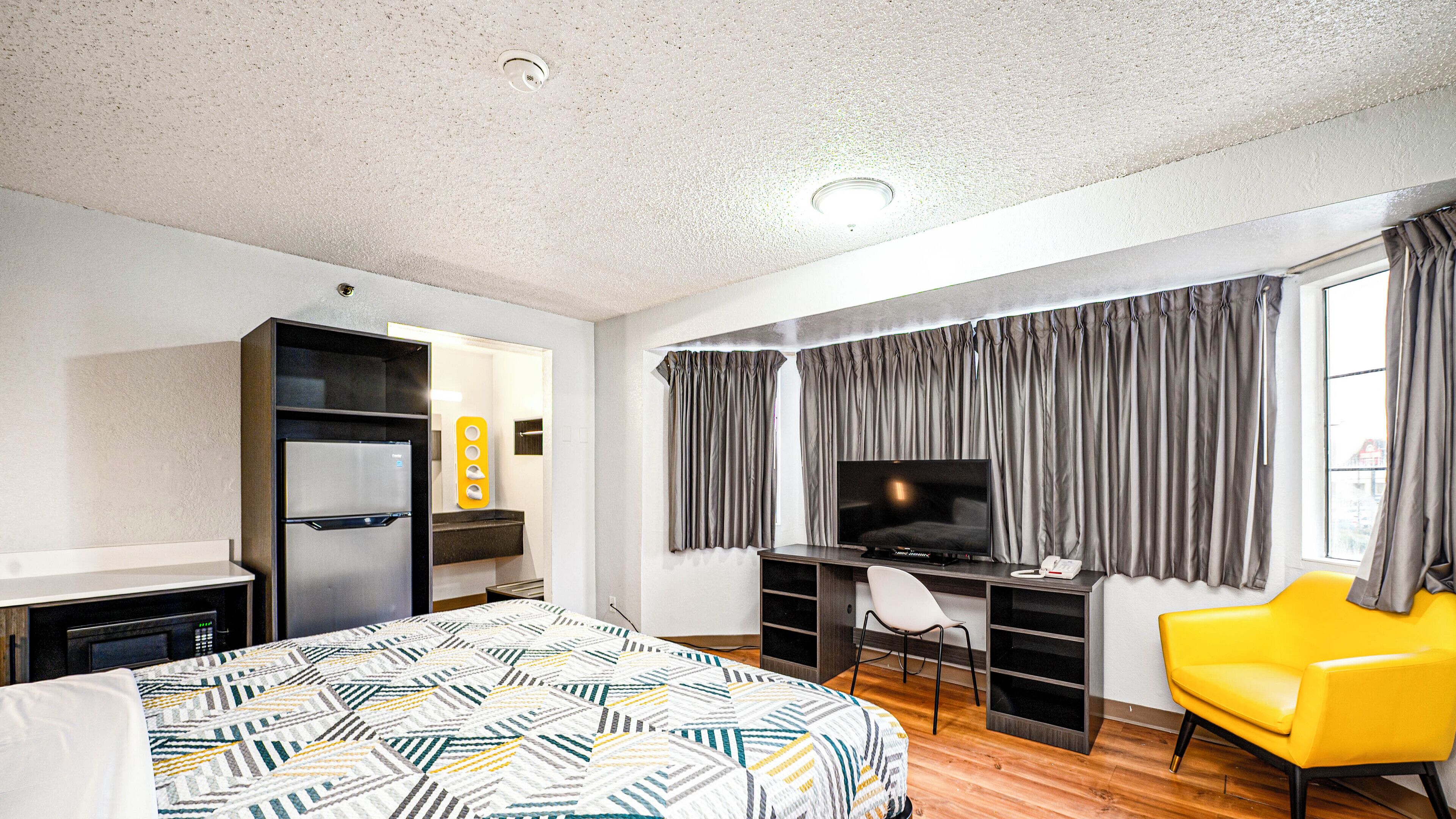A hotel room with a bed, a desk with a computer, a TV, a chair, and a wardrobe.