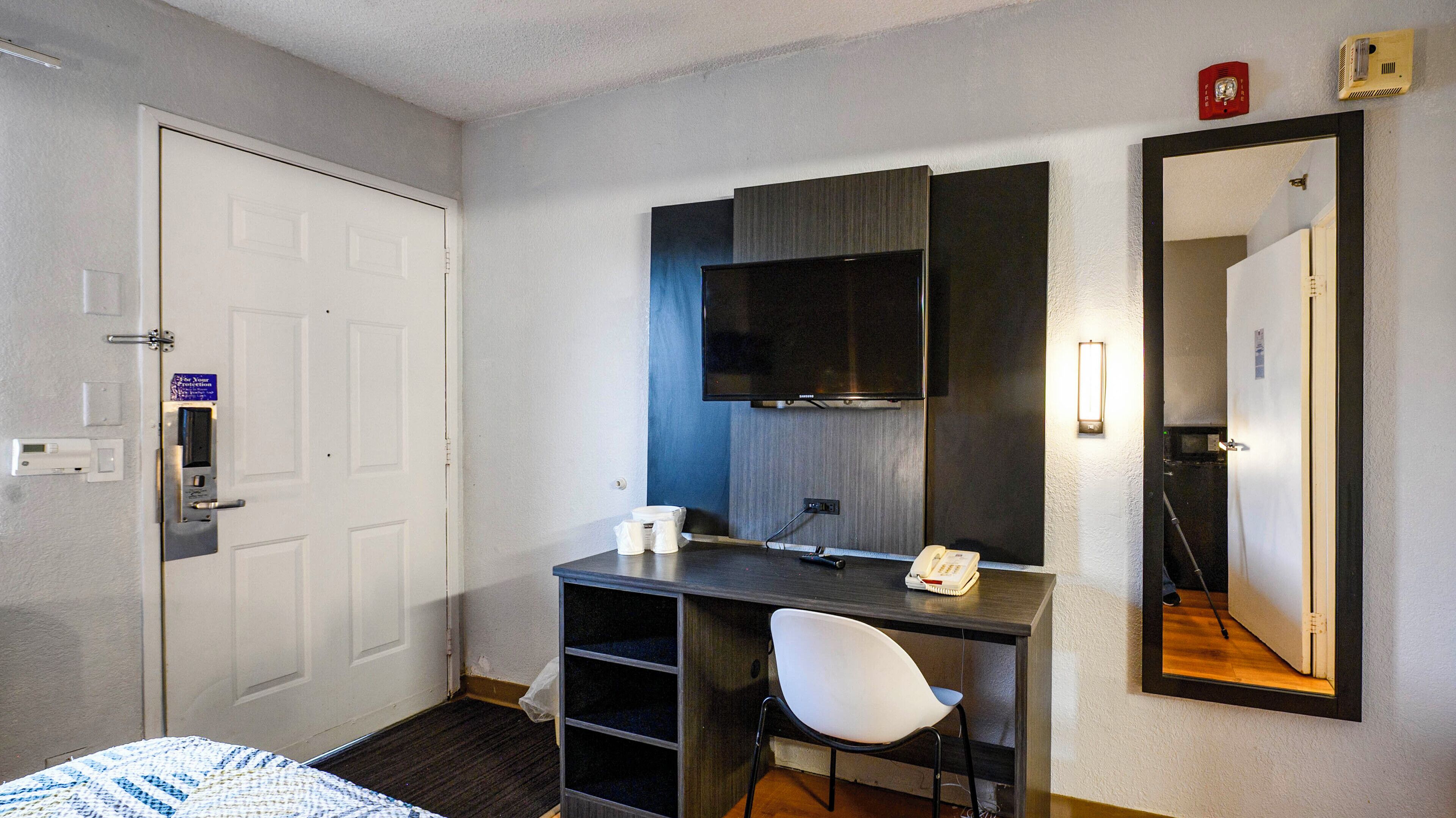 Une chambre d’hôtel comprenant un lit, un bureau avec une chaise, un téléviseur à écran plat, un téléphone et un miroir.