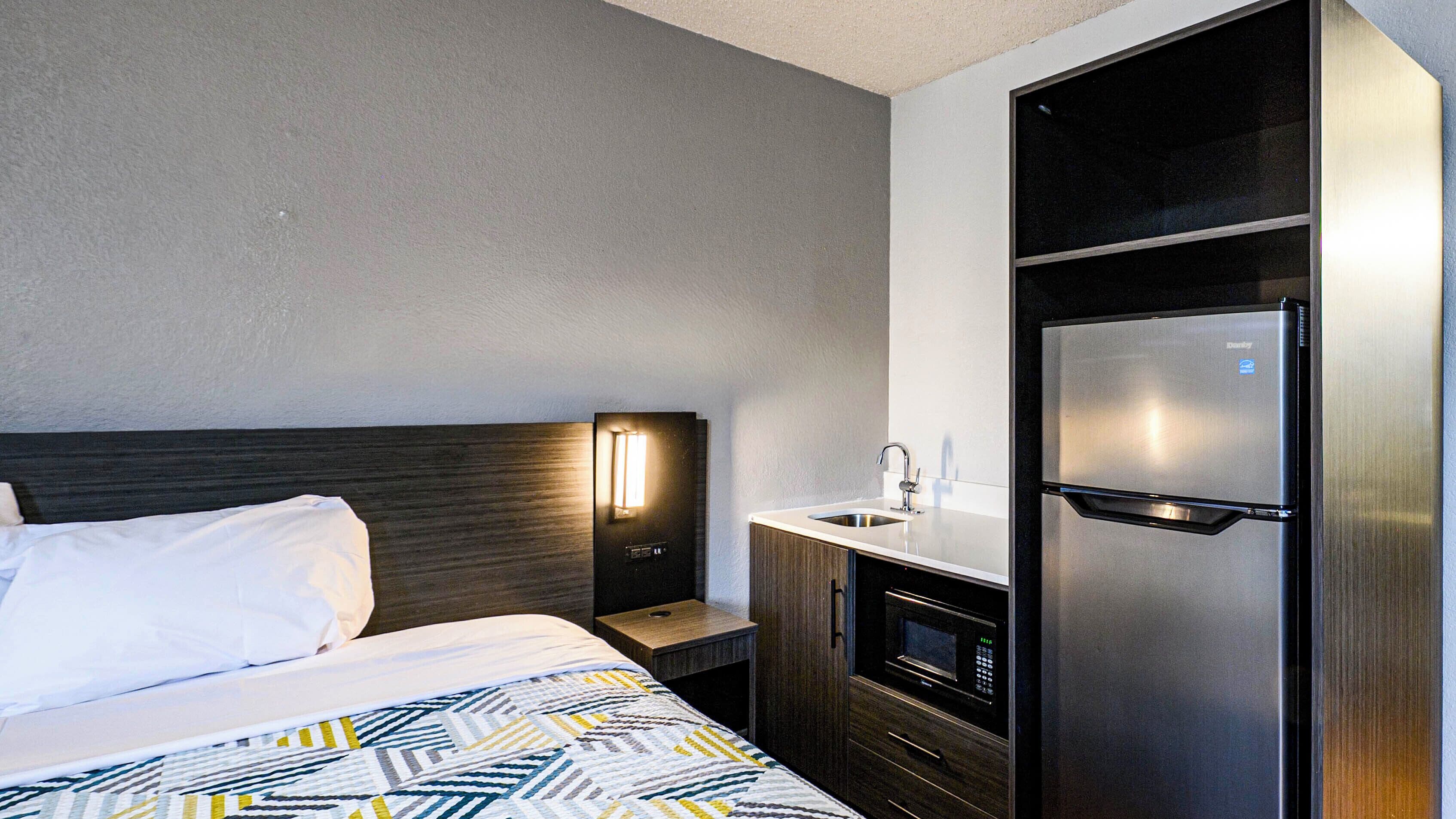 Een hotelkamer met een bed, een nachtkastje, een ingebouwde magnetron en een koelkast.