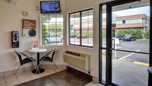 A hotel lobby with a reception desk, two chairs, a television, a window with a view of the parking lot and buildings, and a wall-mounted air conditioner. - Motel 6 Wethersfield, CT - Hartford (Wethersfield)