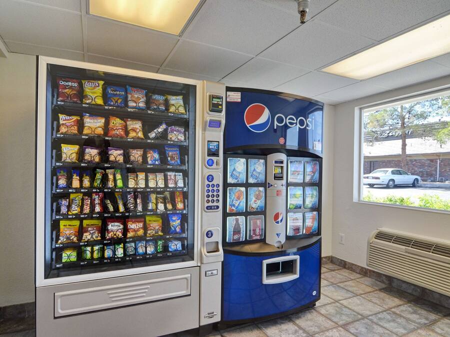Máquina de vendas com lanches e o logotipo da Pepsi, localizada em ambiente interno com vista para a janela.