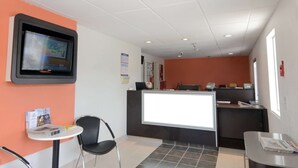 A reception area with a reception desk, a mounted television, and a seating area with chairs and a small table. - Motel 6 Twentynine Palms, CA (Twentynine Palms)