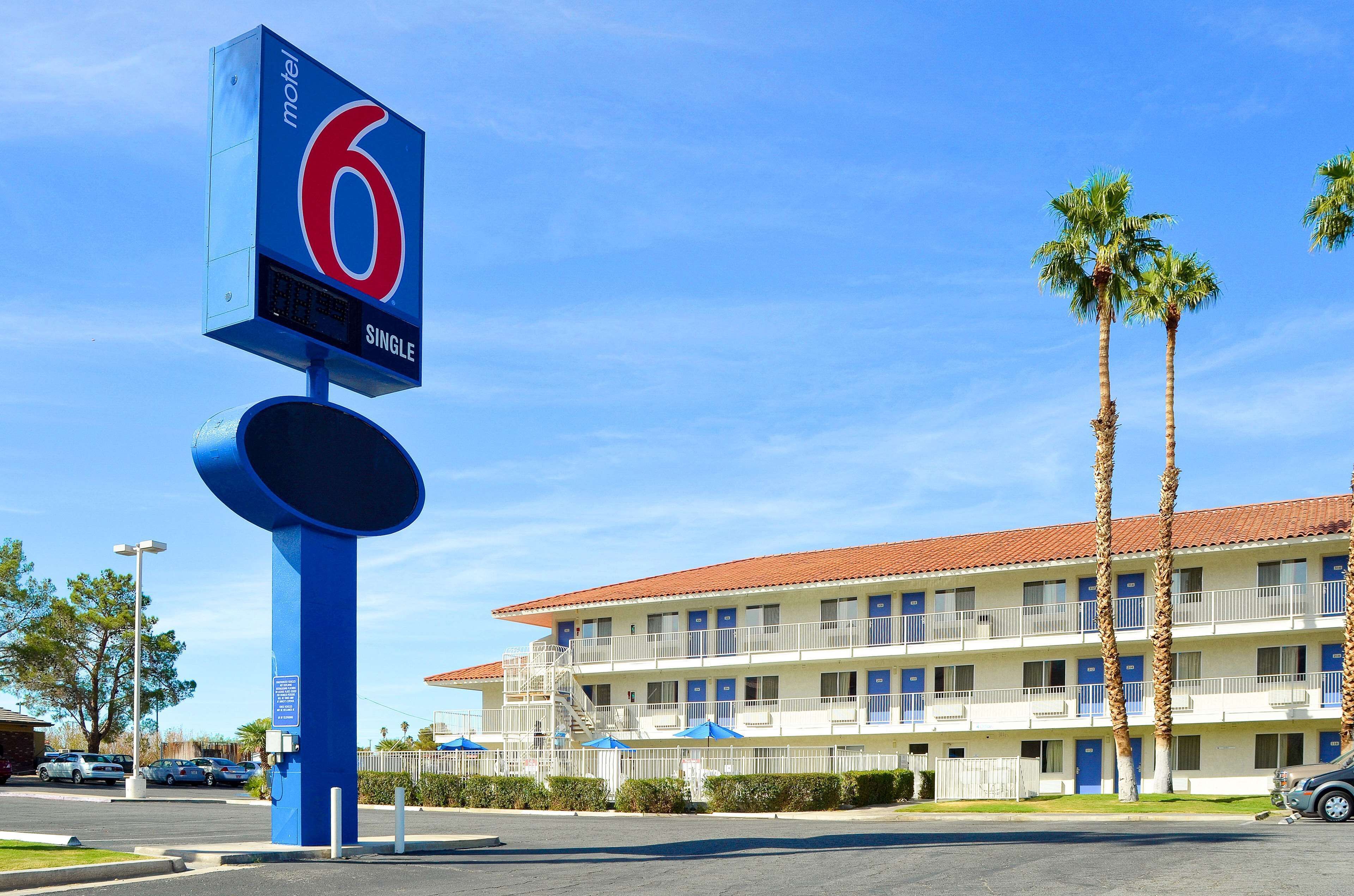 A motel with a prominent sign, a parking lot, and a building with multiple balconies and palm trees.