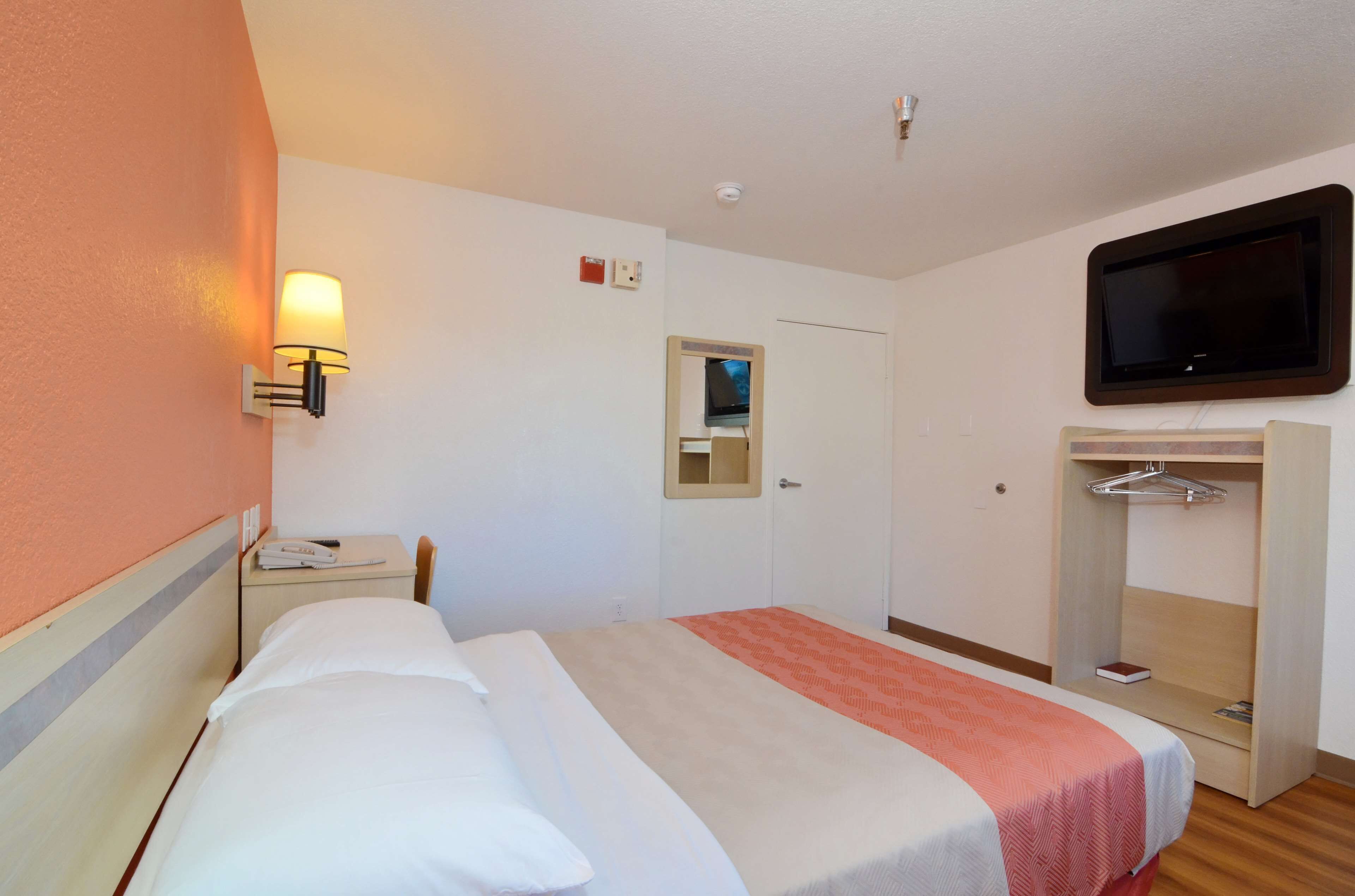 Una habitación de hotel con cama, mesita de noche, lámpara, televisor, espejo y armario.