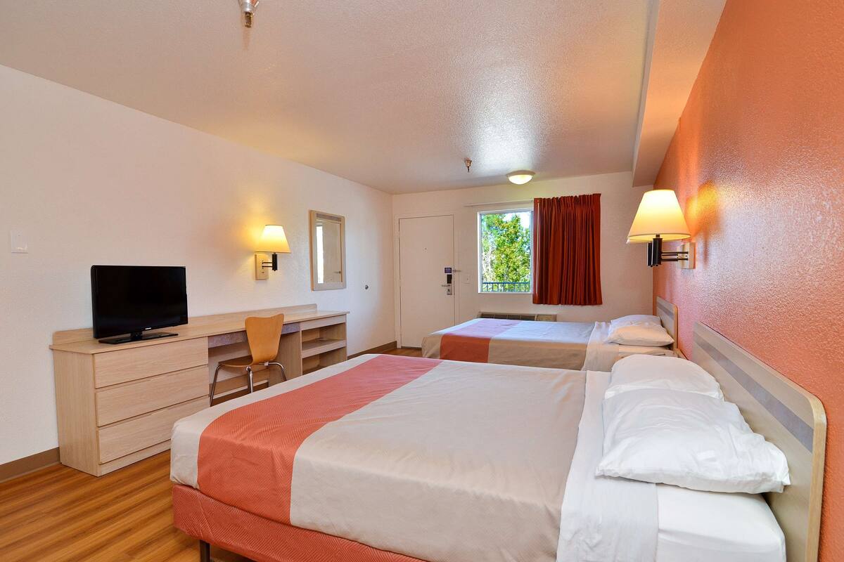 A hotel room with two beds, a desk with a television, and a window with curtains.