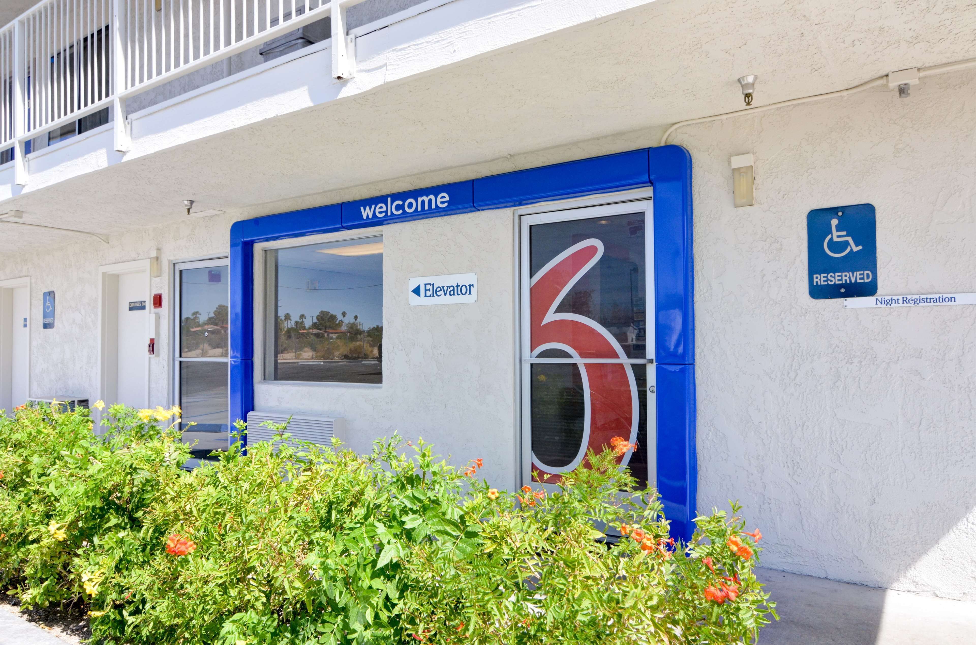 Entrada de un edificio con un cartel de 'welcome', un cartel de ascensor, un cartel con el número '6' y un cartel de 'RESERVED' con el símbolo de una silla de ruedas.