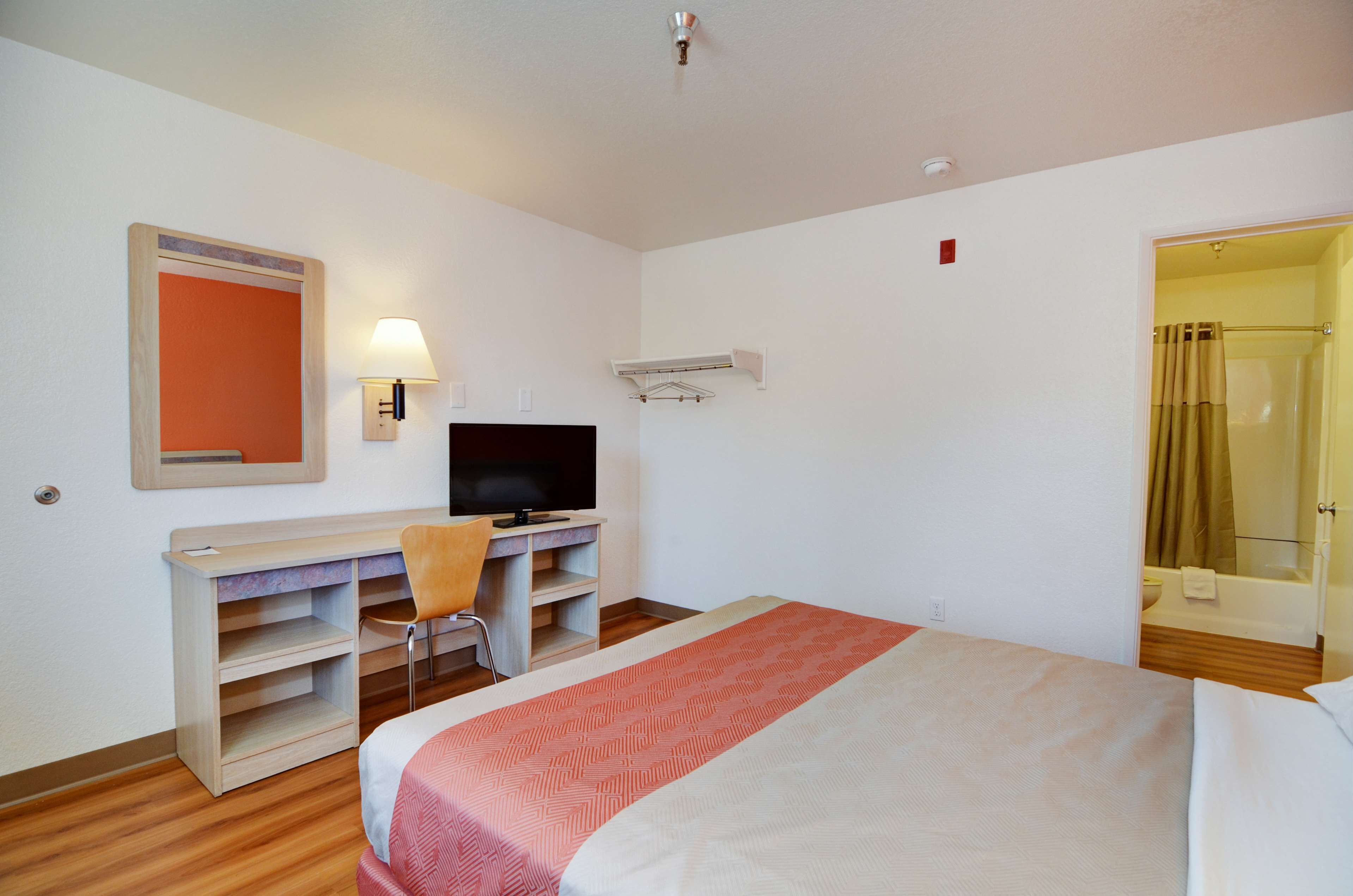 Una habitación de hotel con cama, escritorio, silla, televisor y zona de ducha.