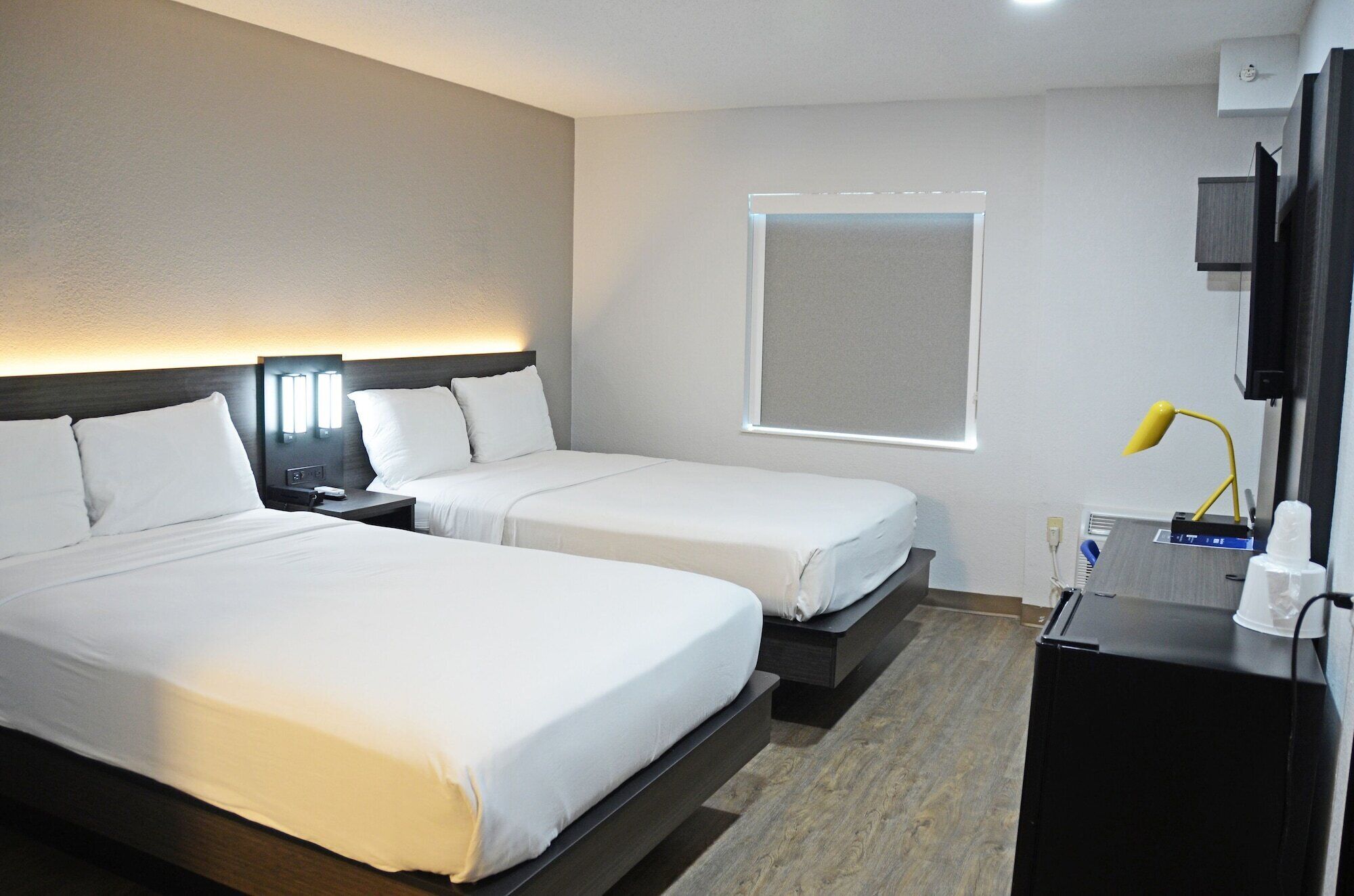 A hotel room with two beds, a TV, a desk, and a window.