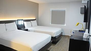A hotel room with two beds, a TV, a desk, and a window.
