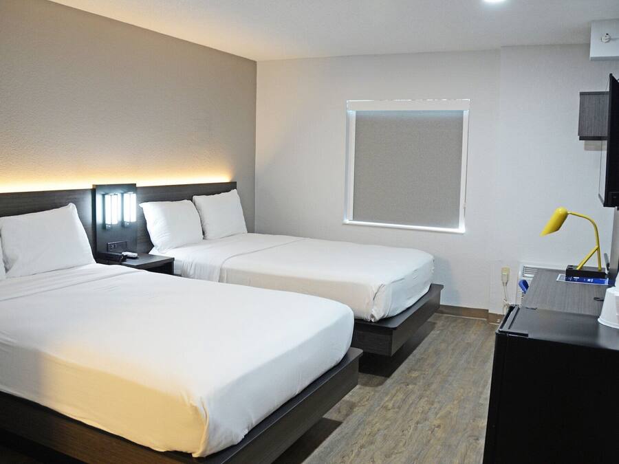 A hotel room with two beds, a TV, a desk, and a window.