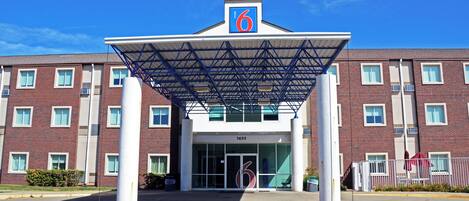 A hotel entrance with a covered walkway, a prominent '6' sign, and a brick building facade.