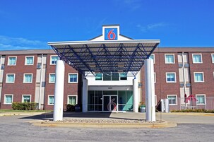Entrada de un hotel con un corredor cubierto, un llamativo letrero con el número '6' y fachada de ladrillo.