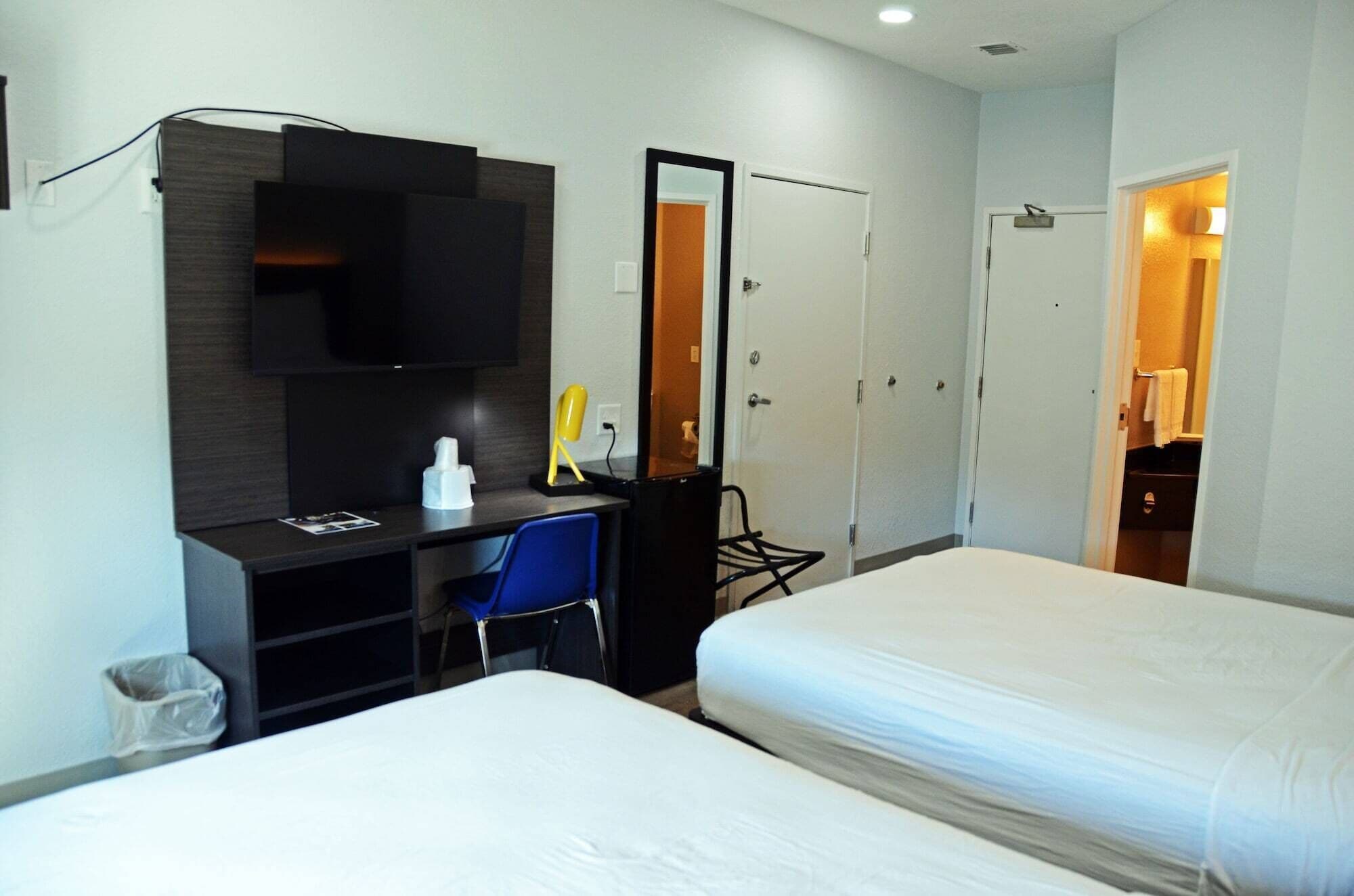 Una habitación de hotel con escritorio, una silla, cama, armario y espejo.