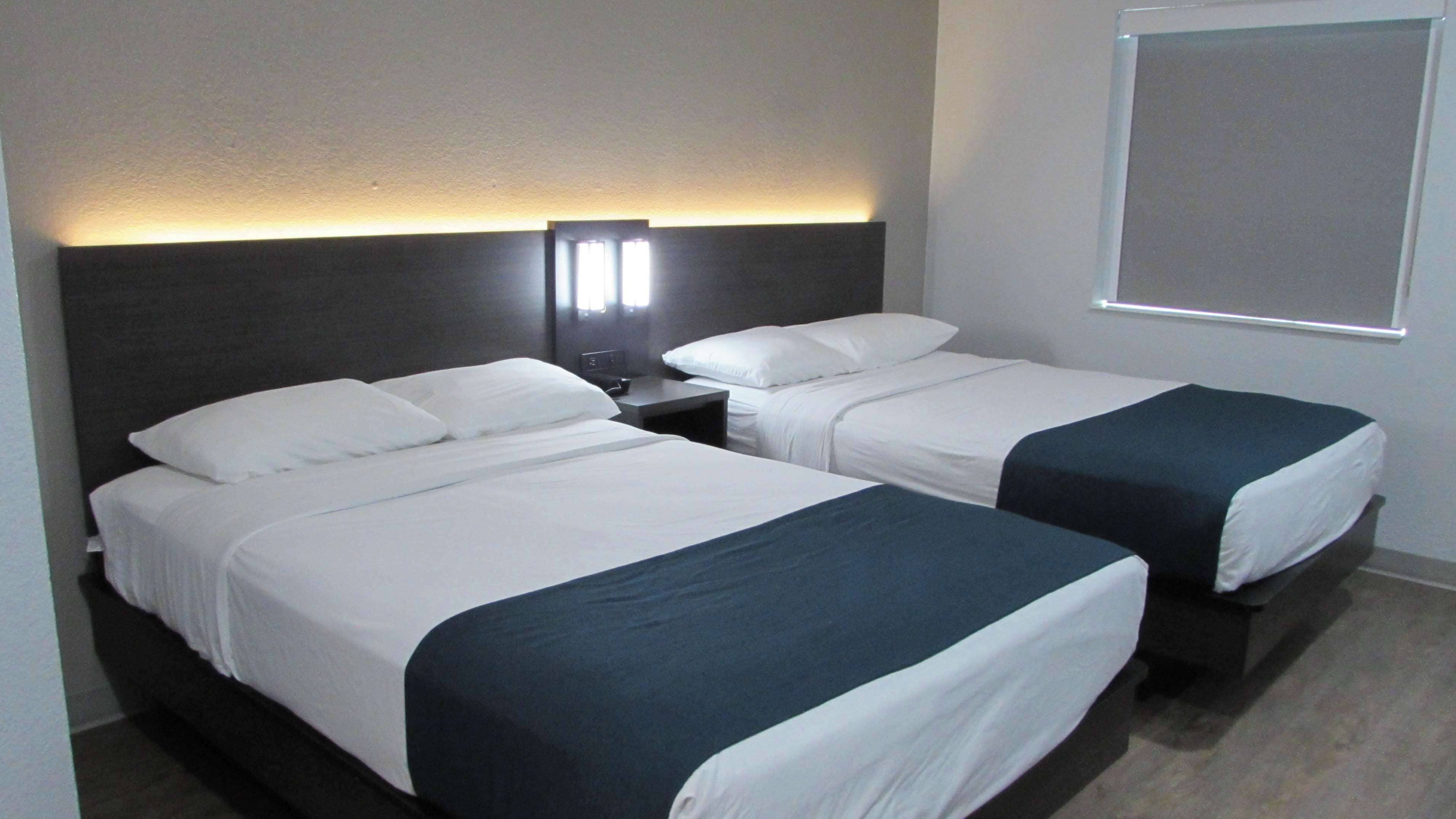 Una habitación de hotel con dos camas individuales, una mesita de noche, una lámpara de pared y una ventana con persianas.