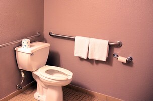 Un baño con inodoro, barra de apoyo y perchero.