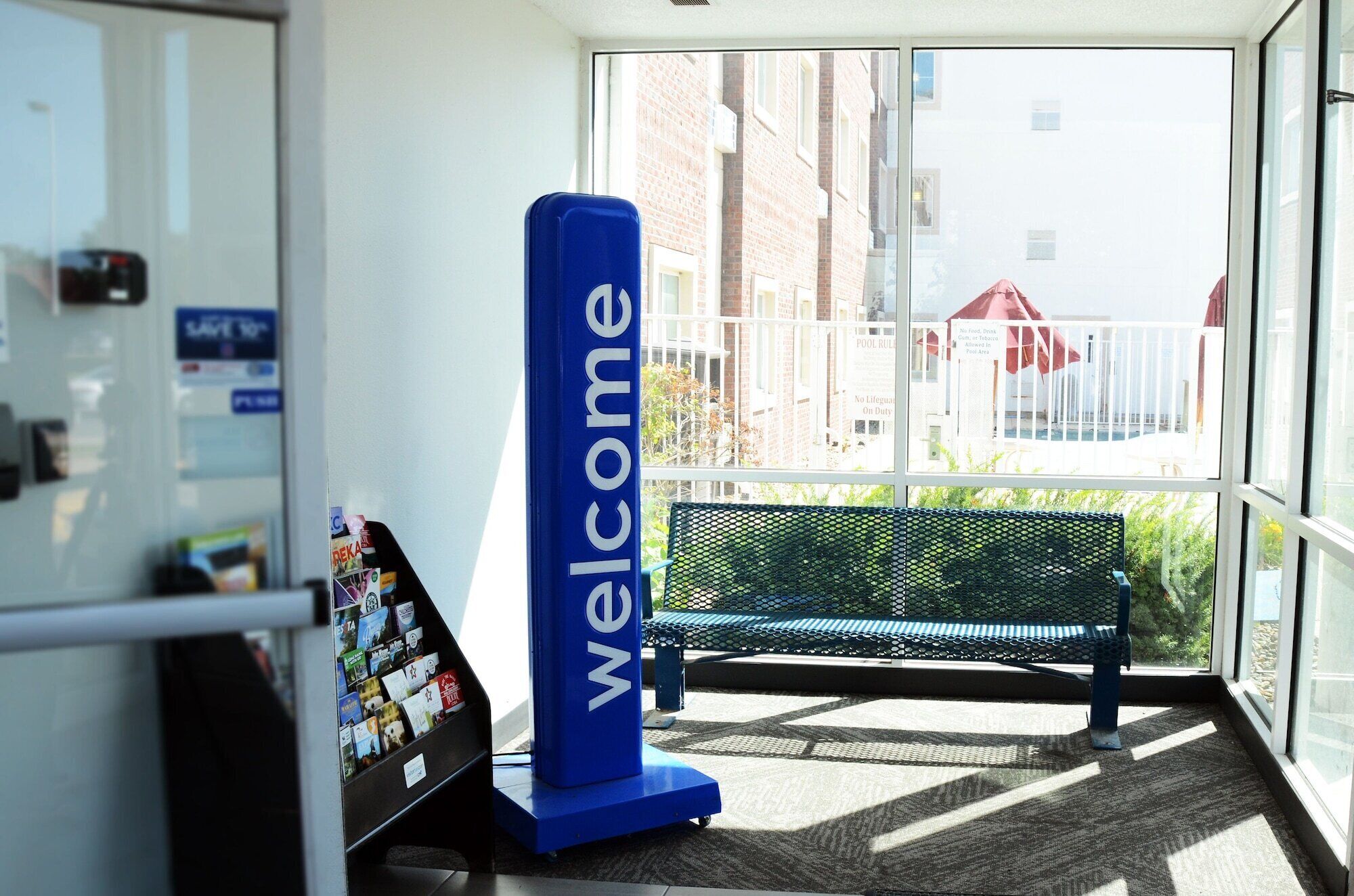 Ein Empfangsbereich mit einem 'Welcome'-Schild, einer Bank und einem Bulletinboard mit verschiedenen Inhalten.