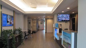 A hotel reception area with a reception desk, chairs, a TV screen, and a poster on the wall. - Motel 6 West Des Moines, IA (West Des Moines)
