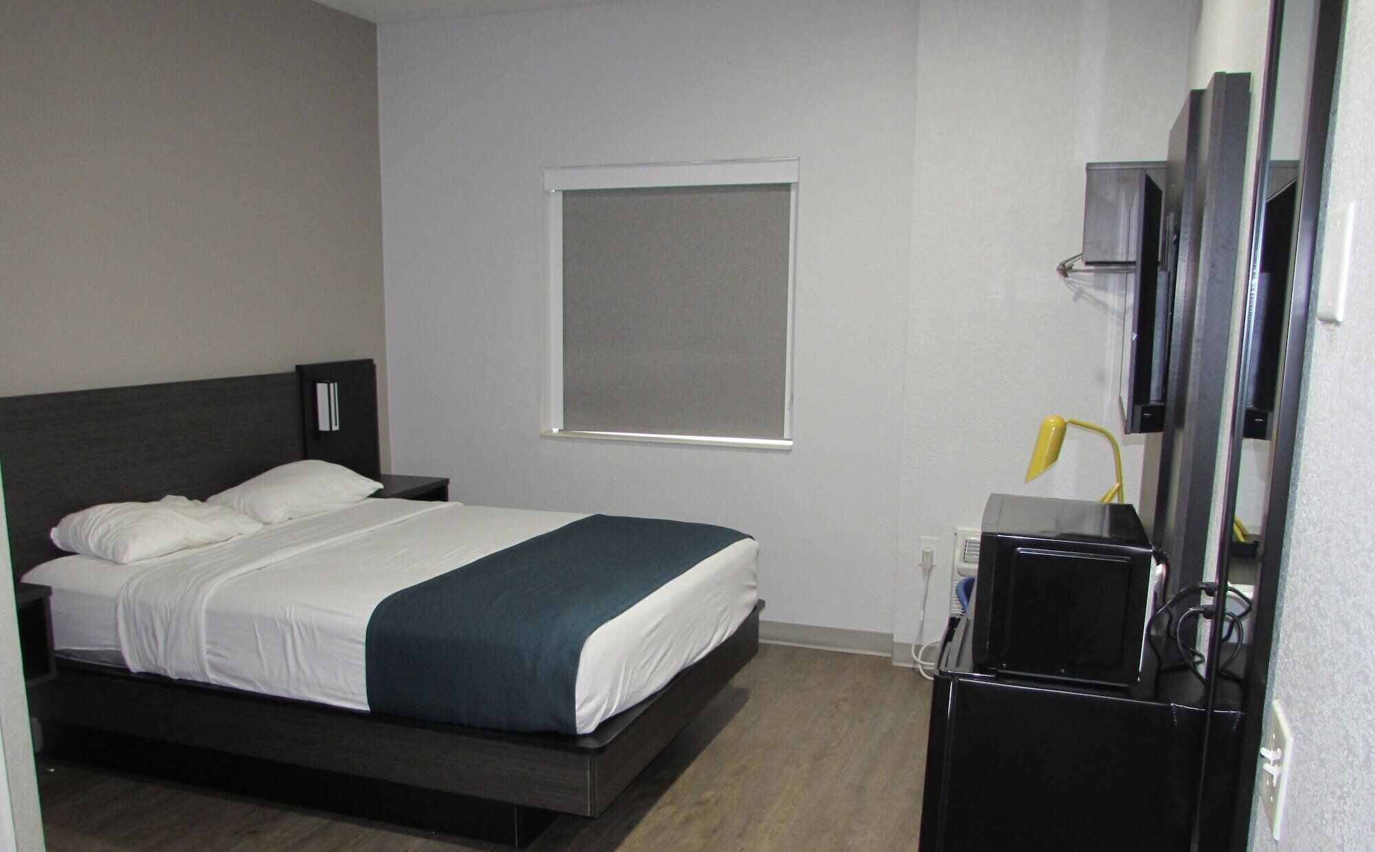 Een hotelkamer met een bed, nachtkastje, televisie en raam.