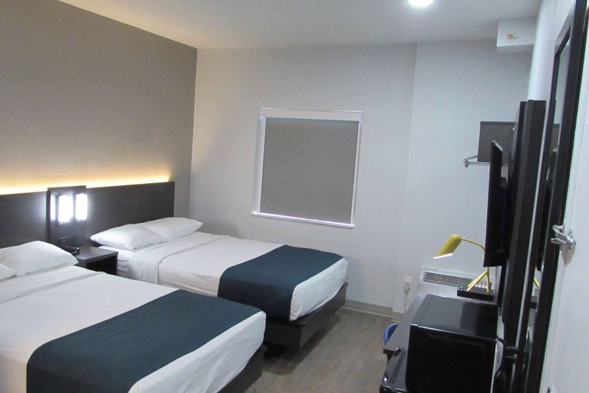 A hotel room with two beds, a desk, a TV, and a window.