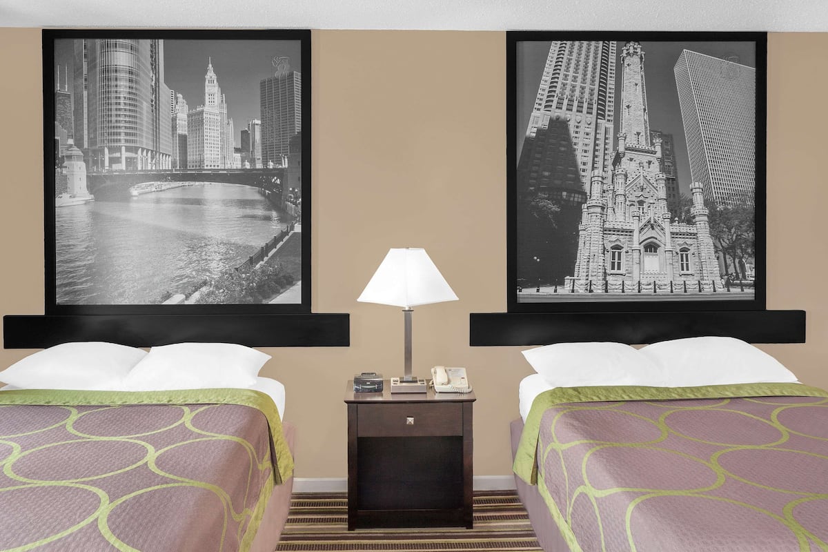 Een hotelkamer met twee bedden, een nachtkastje met een lamp, en twee stadsgezichten in lijsten aan de muur.