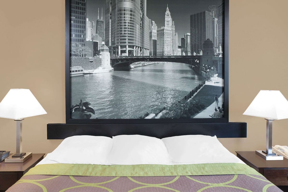 Hotelkamer met een bed, twee bedlampen, een nachtkastje met een telefoon en een groot stadsgezichtschilderij aan de muur.