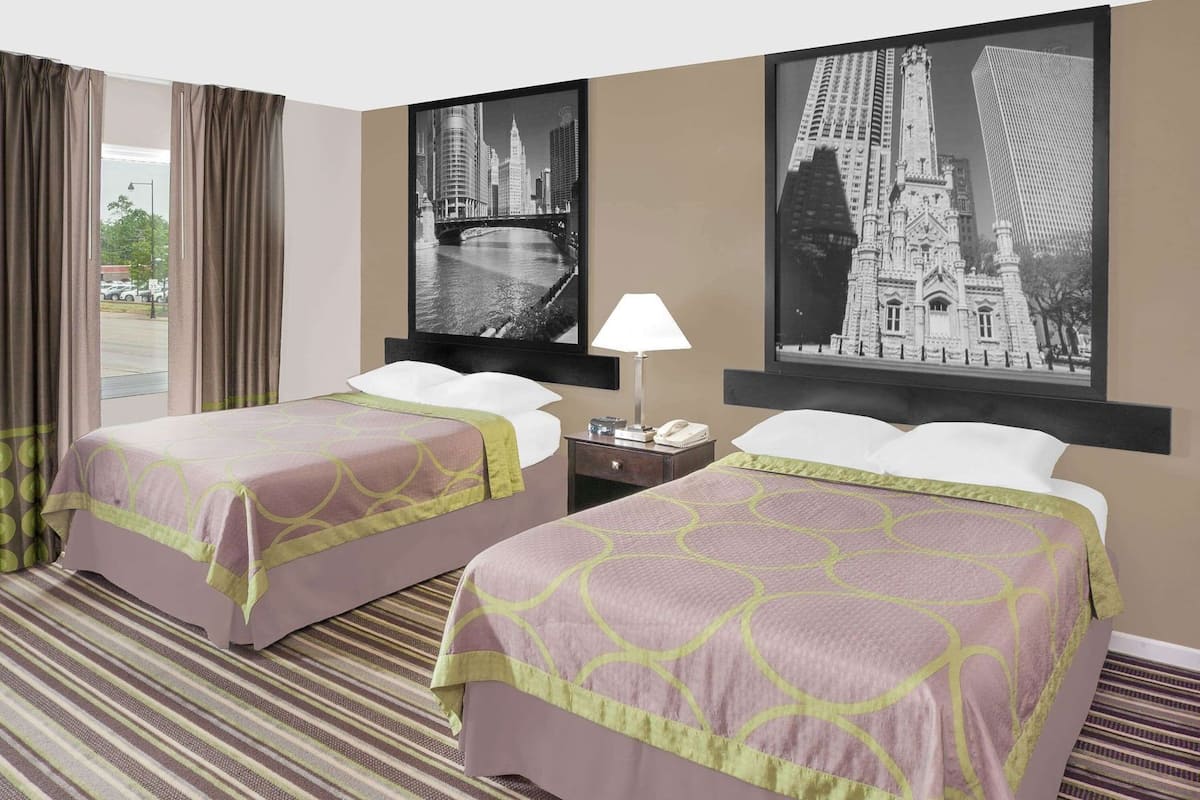 Een hotelkamer met twee bedden, een nachtkastje, een lamp en twee grote zwart-wit foto’s van een stadsgezicht aan de muur.