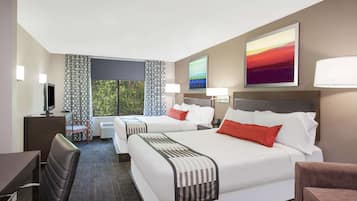 A hotel room with two beds, a desk, a chair, a TV, and a window with curtains.