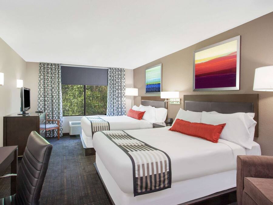 A hotel room with two beds, a desk, a chair, a TV, and a window with curtains.