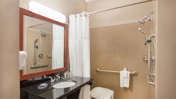 A bathroom with a sink, mirror, shower, and a small white stool.