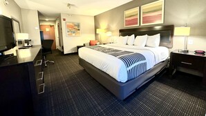 Ein Hotelzimmer mit einem großen Bett, einem Schreibtisch mit Flachbildfernseher, einem Sessel, einer Schreibtischlampe und einem Nachttisch mit Lampe.