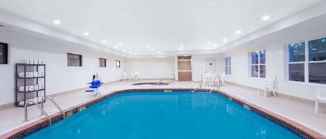 Ein Hallenbad mit klarem Wasser, umgeben von weißen Wänden und einem gefliesten Boden.