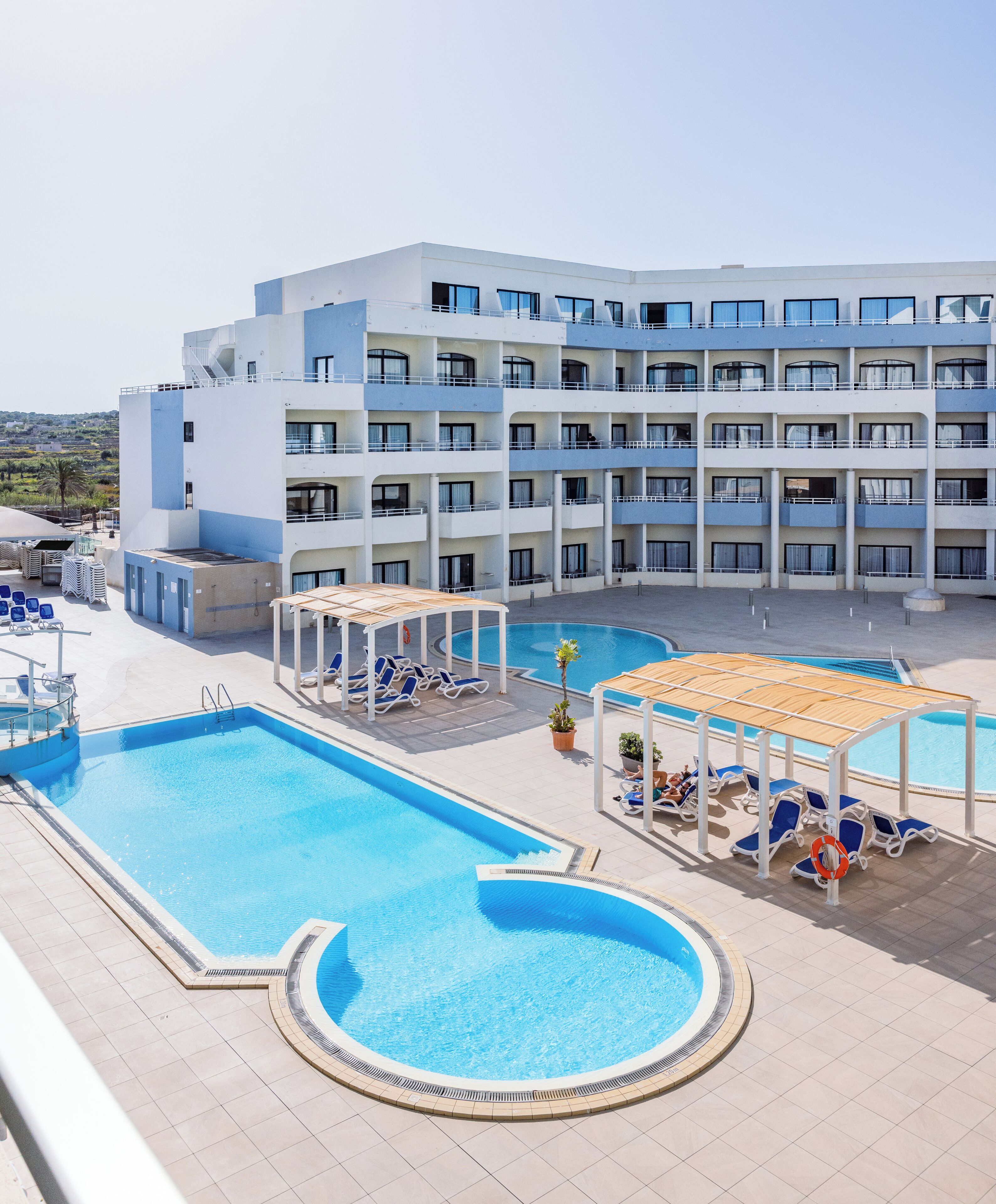 Et hotel med flere swimmingpools, liggestole og en stor bygning med altaner.