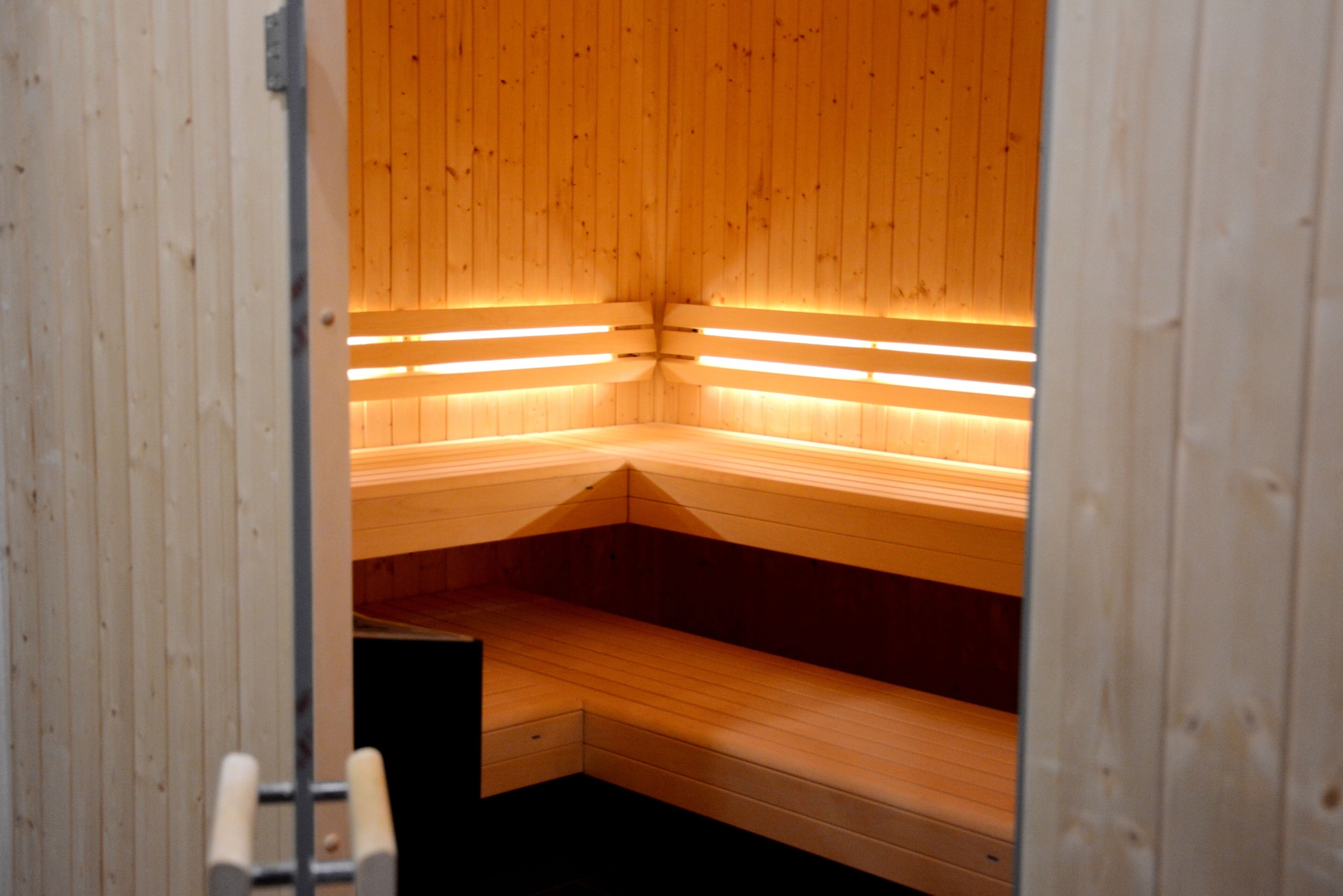Een sauna met houten banken en inbouwbanken, een ladder en een deur.