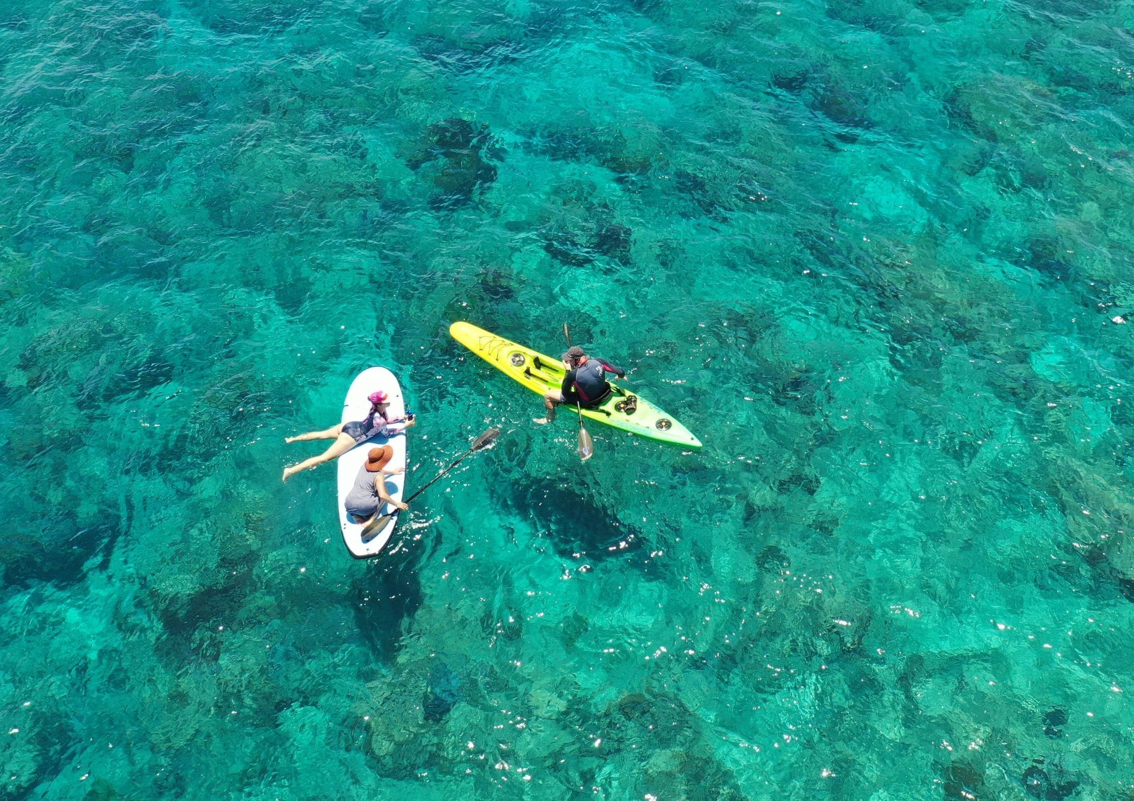 A clear view of a turquoise sea with two kayaks and a paddleboard.