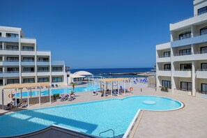 A hotel pool area with multiple levels of balconies, a clear view of the sea, and sun loungers.