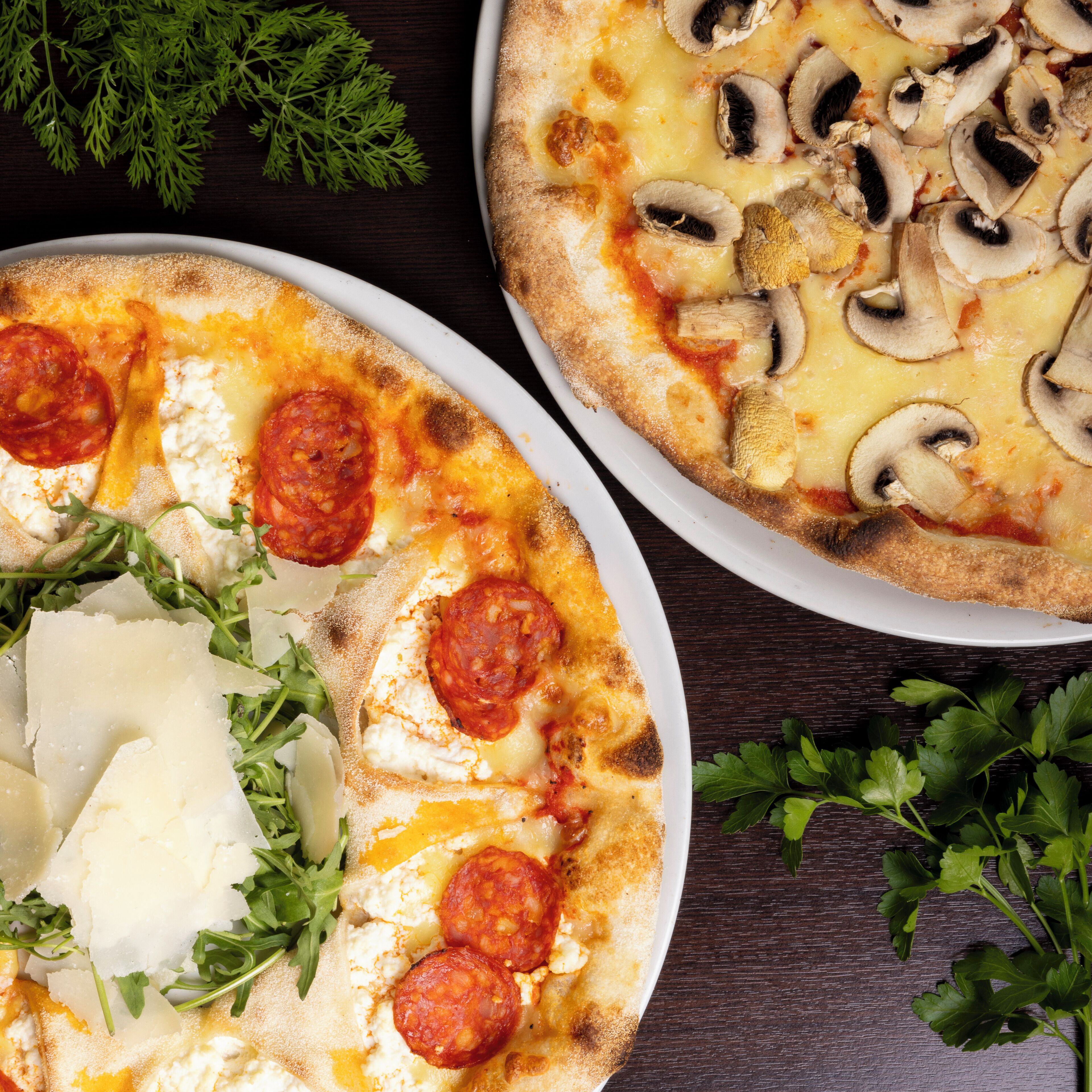 Dos pizzas con diferentes ingredientes, adornadas con hierbas, sobre una mesa de madera.